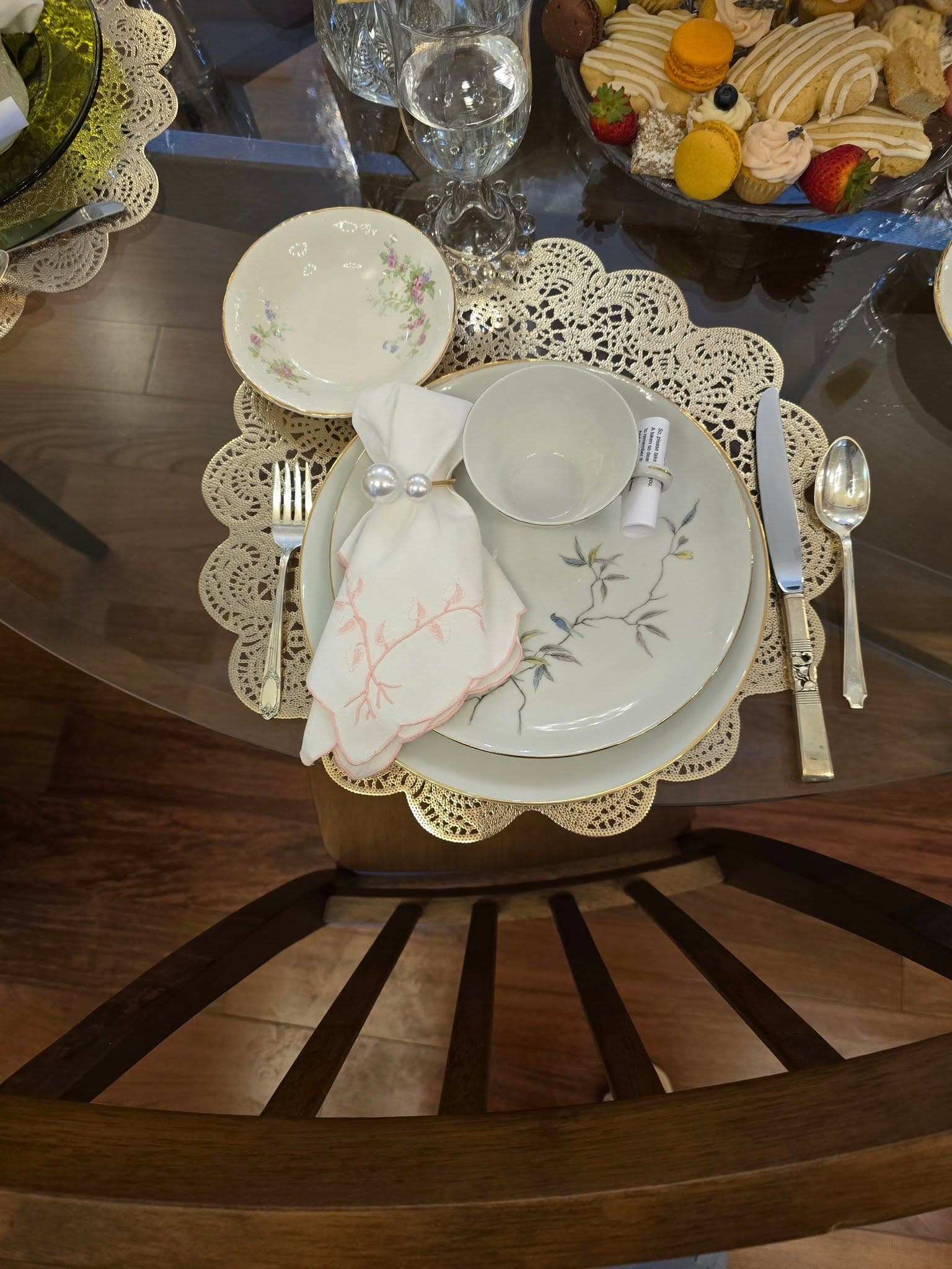 Floral china teacup and plates with an embroidered napkin, pearl napkin ring, and lace placemat