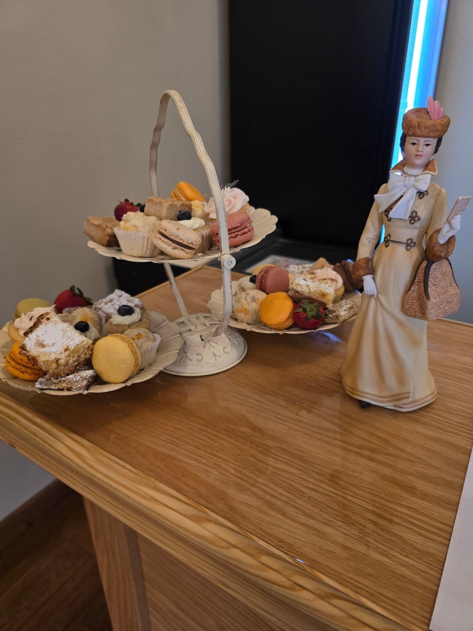 Tiered display of macarons, miniature cupcakes, and pastries beside a decorative figurine