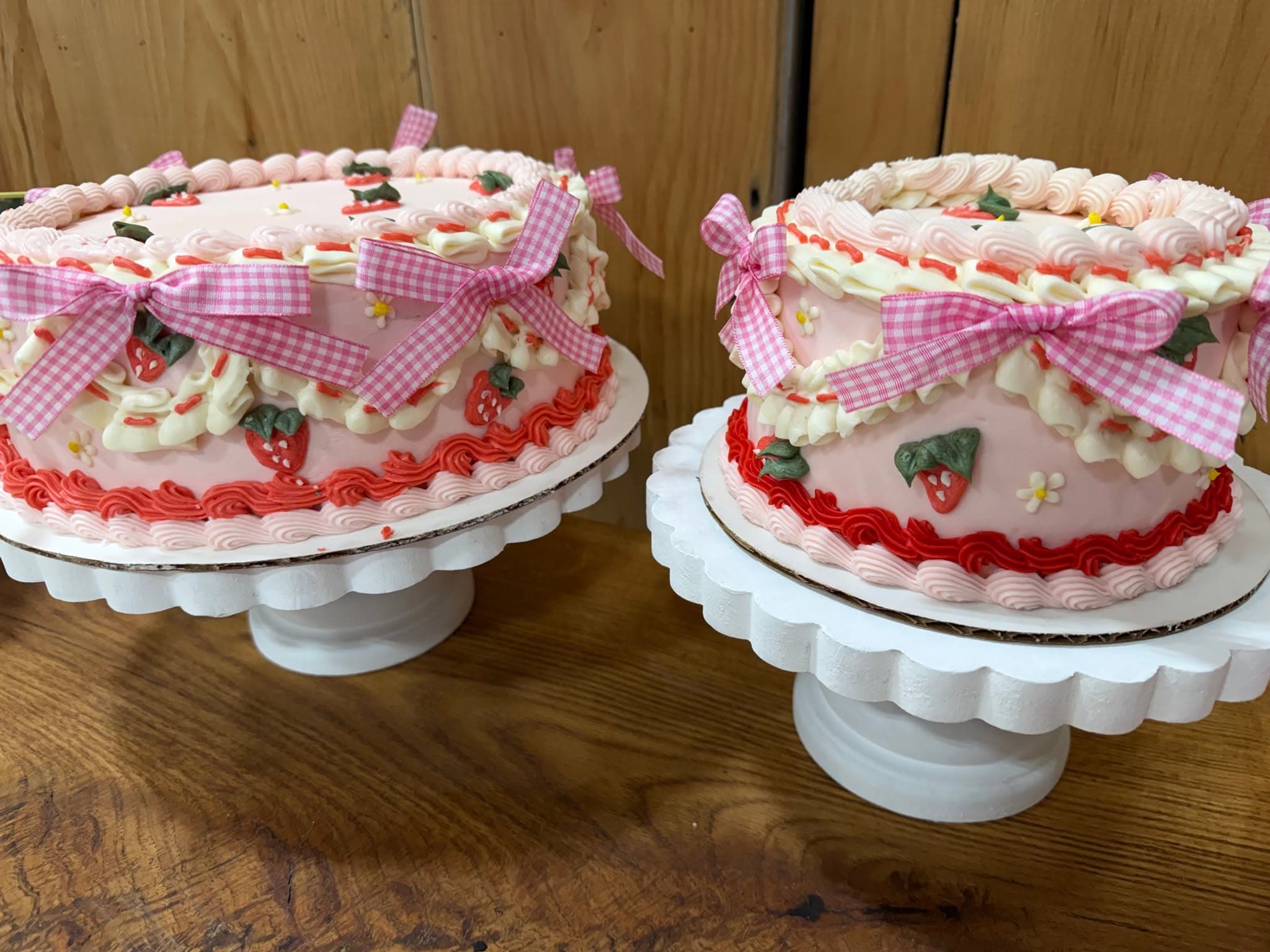 Pink celebration cakes with piped strawberries, buttercream swirls, and gingham bows.